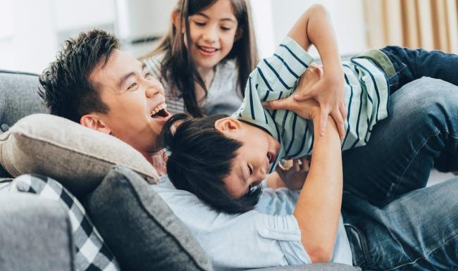 father plays on a couch with his young children